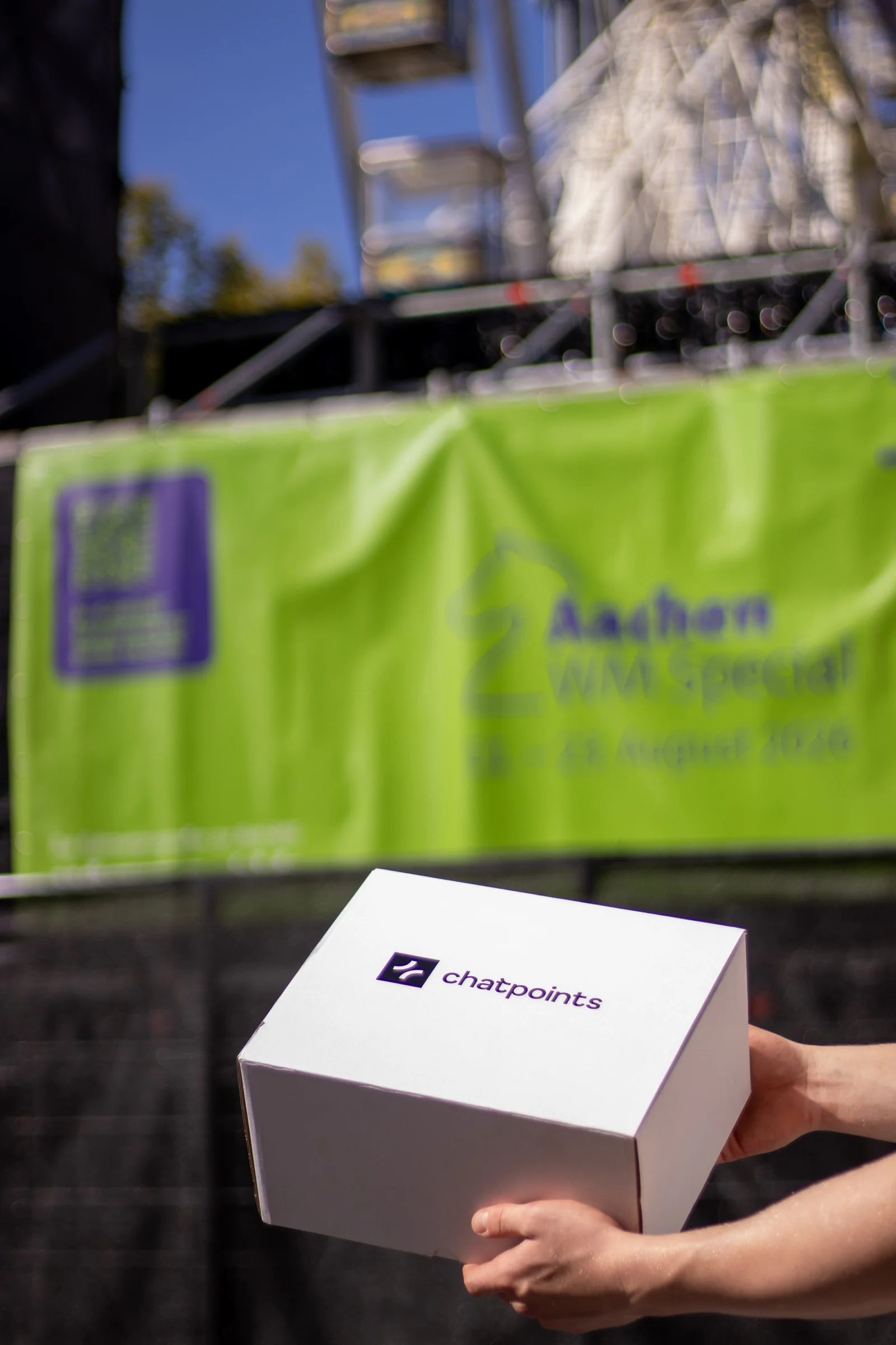 Hände tragen eine weiße chatpoints-Box vor dem Aachen-WM-Special-Banner und dem Riesenrad