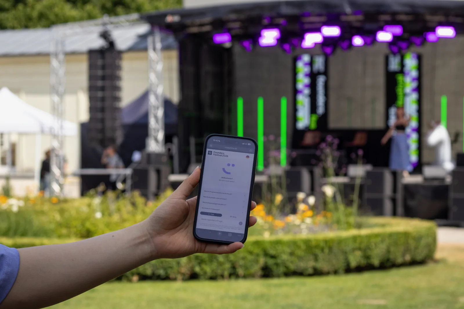 Ein Smartphone mit dem chatpoints-Assistenten vor der Bühne des founders.festival 2026 in Aachen