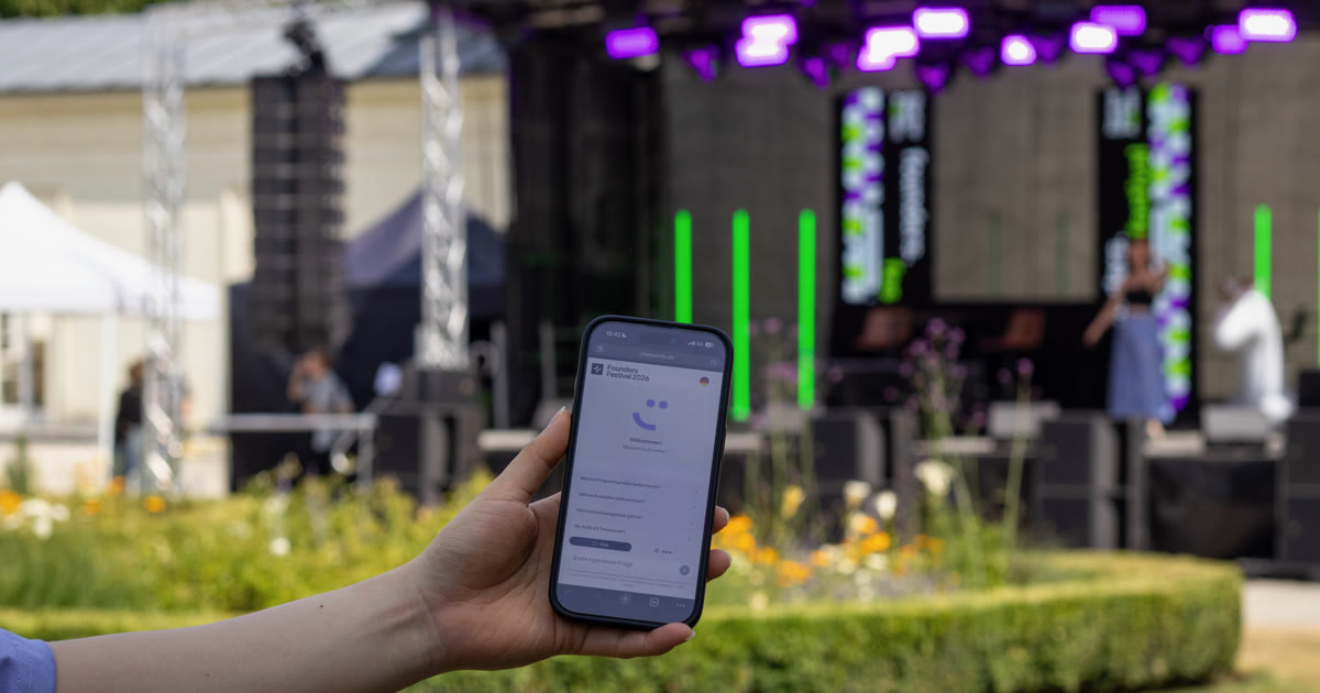 Ein Smartphone mit dem Festival-chatpoint vor der Bühne des founders.festival 2026