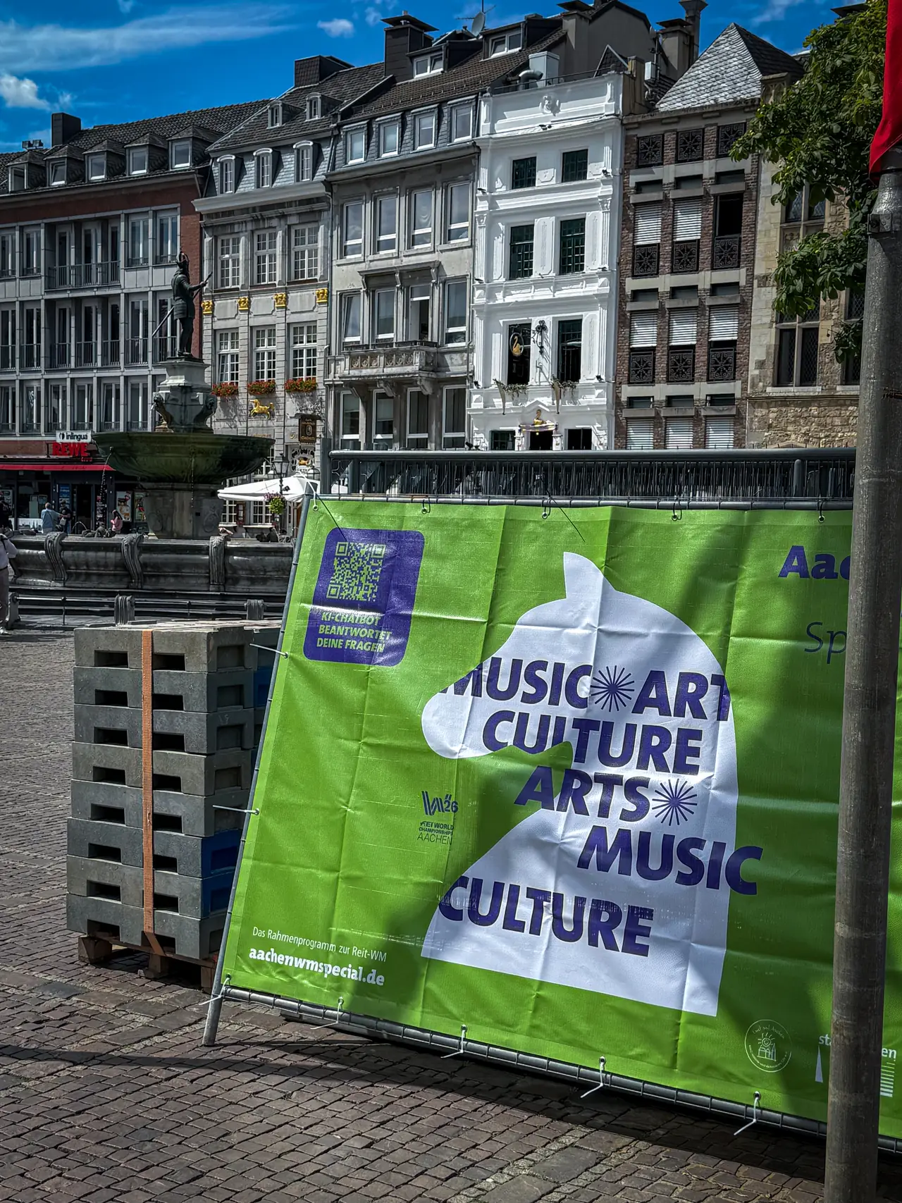 Grünes Aachen-WM-Special-Banner mit violettem QR-Code auf dem Aachener Markt