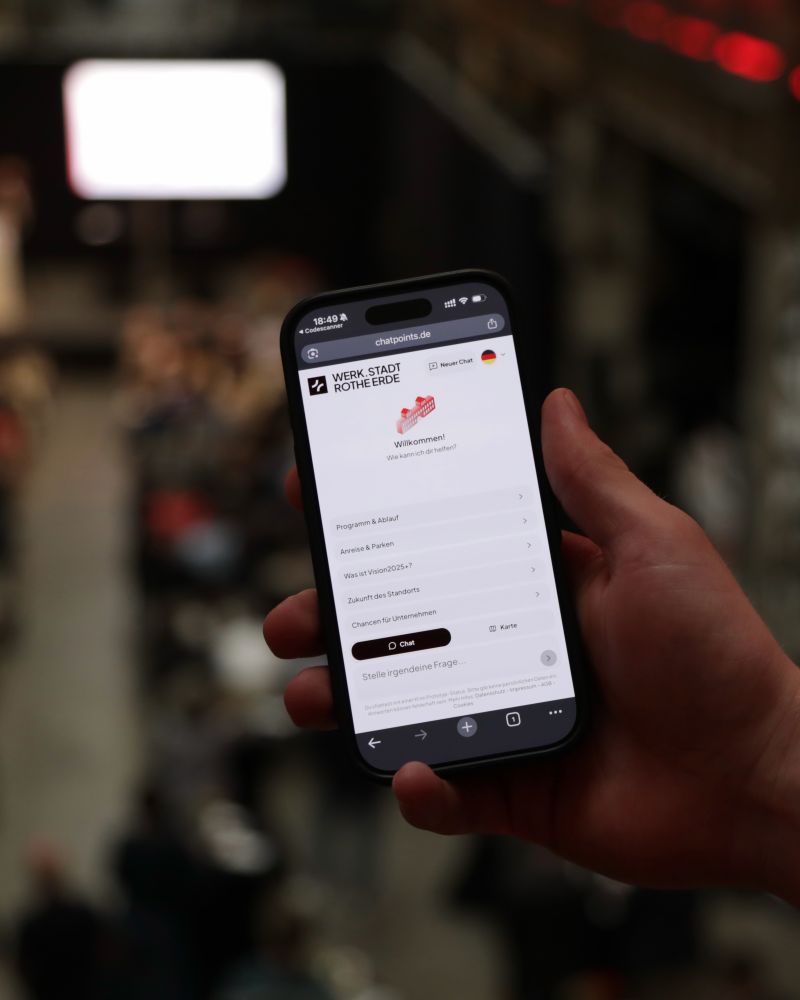 Smartphone mit dem digitalen WERK.STADT ROTHE ERDE Guide vor der beleuchteten Stranghalle